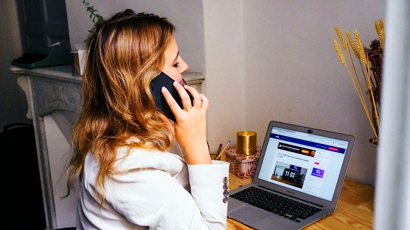 Eine Person telefoniert an ihrem Schreibtisch, daneben ein aufgeklapptes Notebook