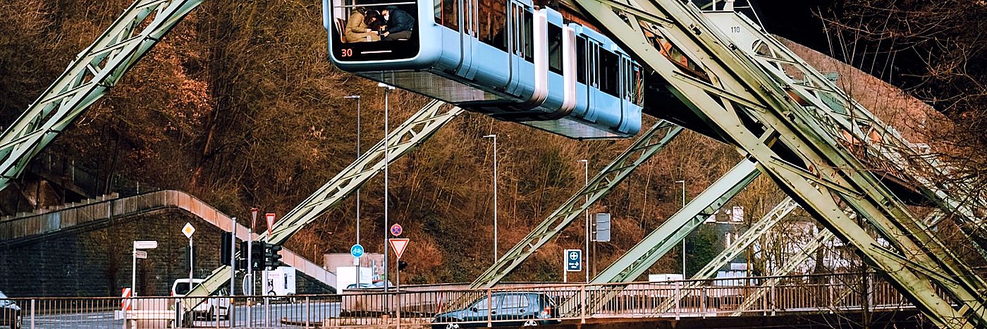 Die Wuppertaler Schwebebahn fährt über der Straße durch das Tal der Wupper